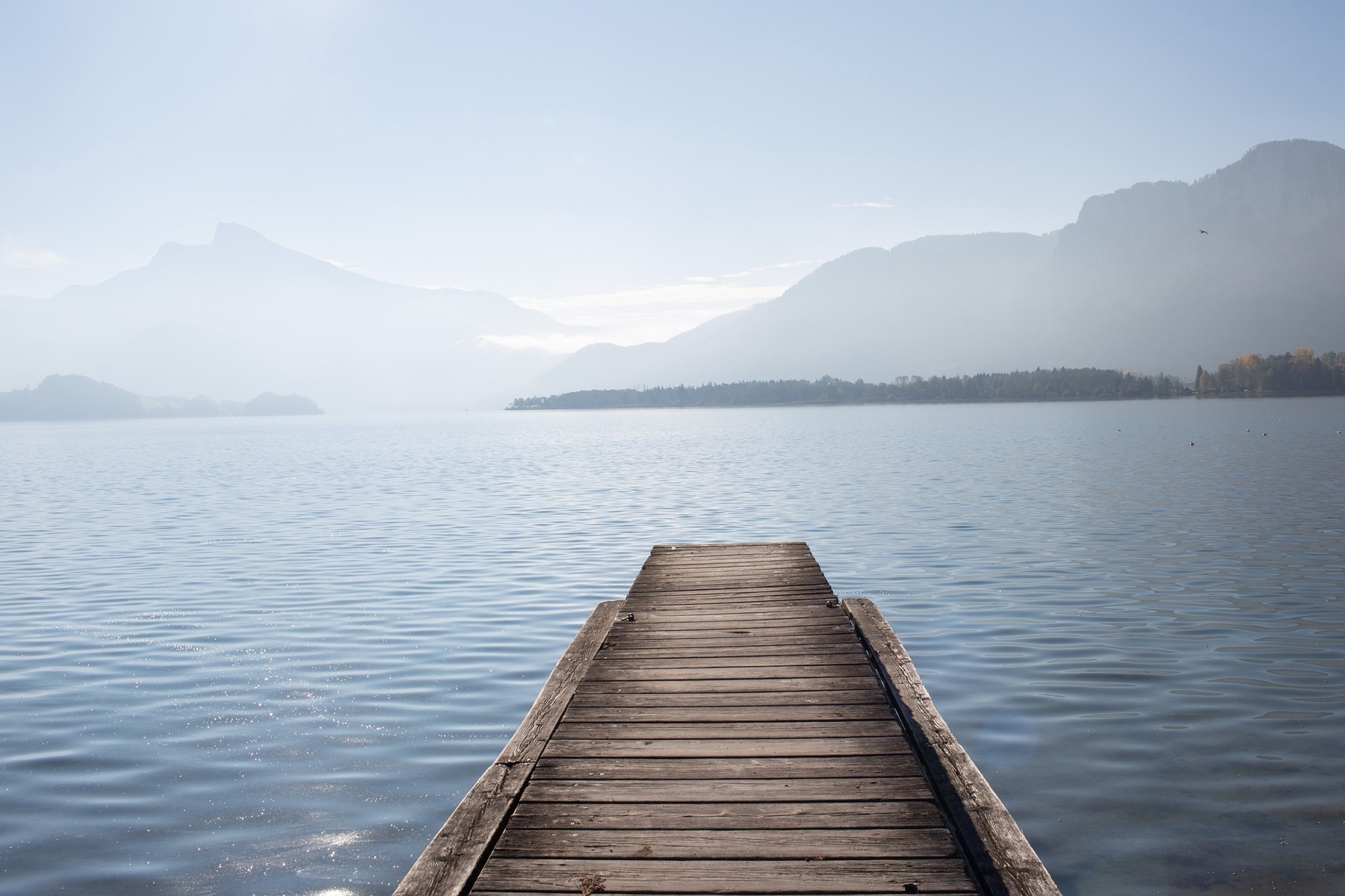 Ponton en bois sur un lac calme, montagnes en arrière-plan